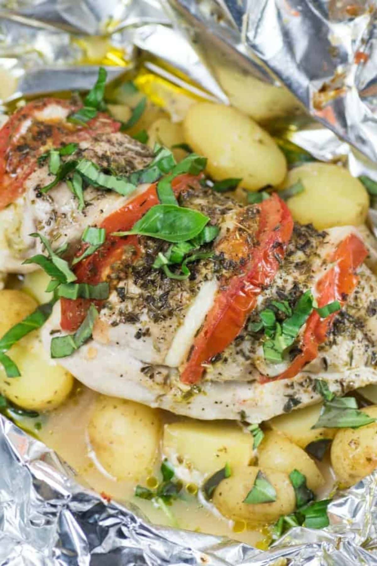 Caprese chicken on top of potatoes in foil.