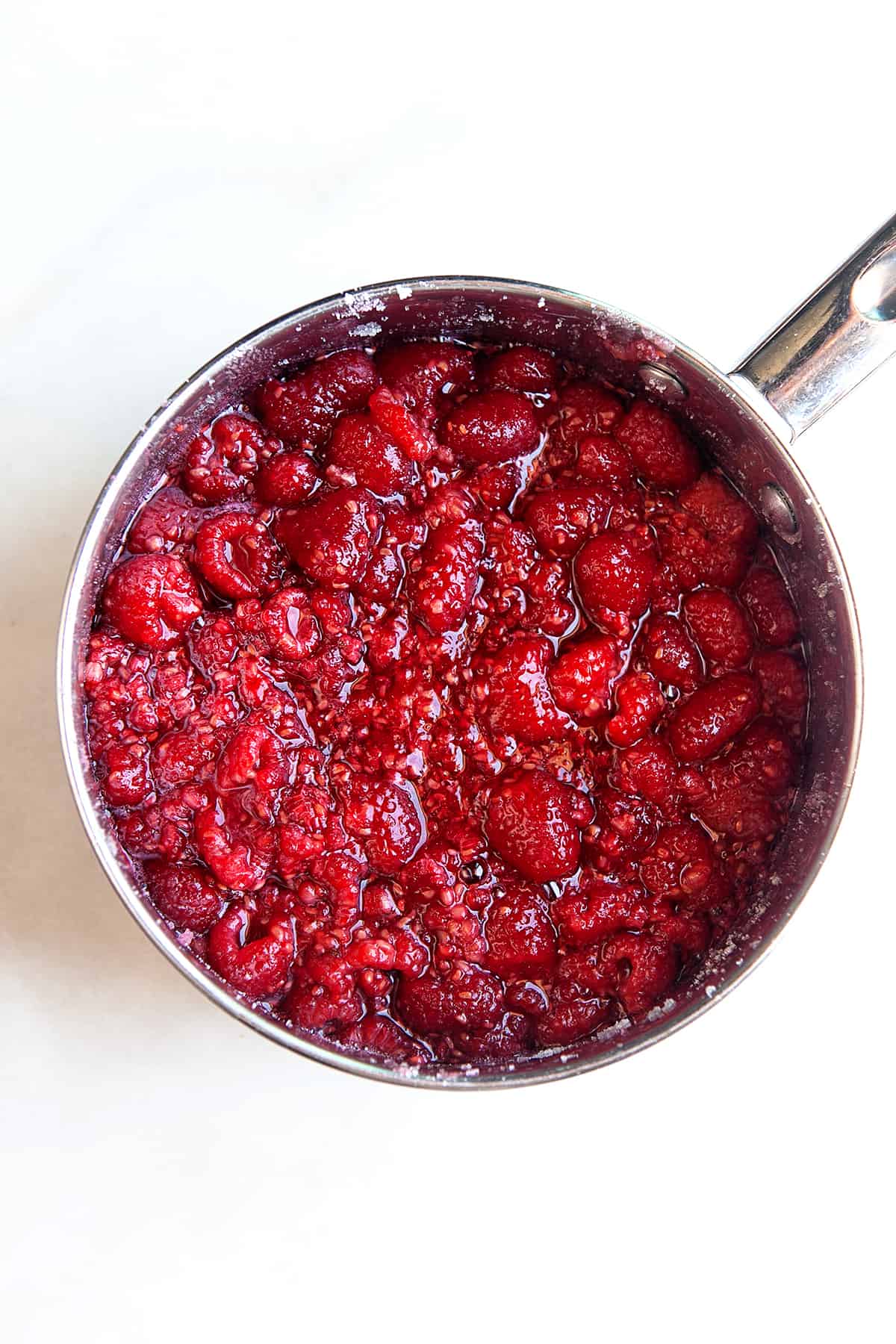 Pot full of raspberries with sugar that is starting to cook. 